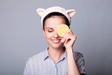 Gri arka planda kozmetik sünger tutan ve gülümseyen güzel bir kadın görüntüsü.