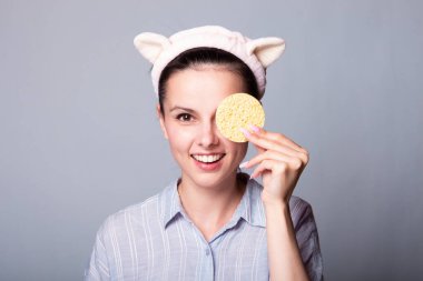 Gri arka planda süngerleri tutarken güzel, gülümseyen genç bir kadın eğleniyor.