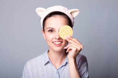 Gri arka planda süngerleri tutarken güzel, gülümseyen genç bir kadın eğleniyor.