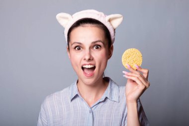 Gri arka planda kozmetik sünger tutan ve gülümseyen güzel bir kadın görüntüsü.