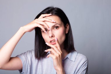 Kadın elleriyle yüzüne dokunuyor, gri stüdyo geçmişi var.