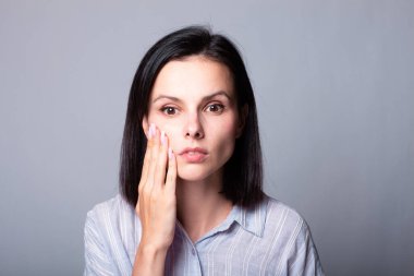 Kadın elleriyle yüzüne dokunuyor, gri stüdyo geçmişi var.