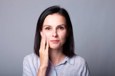 Kadın elleriyle yüzüne dokunuyor, gri stüdyo geçmişi var.