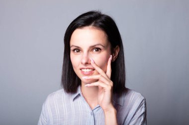 Kadın elleriyle yüzüne dokunuyor, gri stüdyo geçmişi var.