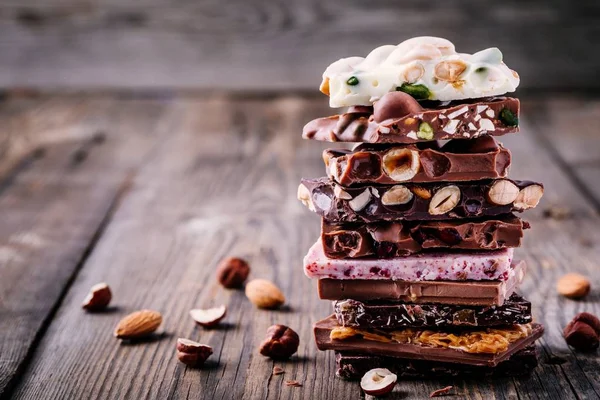 ホワイト ミルク ナッツ キャラメル フルーツと木製の素朴な背景にベリー風味のダーク チョコレートのスタック — ストック写真