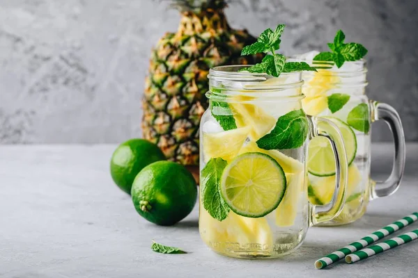 Infused detox water with pineapple, lime and mint. Ice cold summer cocktail or lemonade in glass mason jar