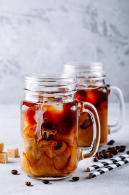 Gri bir arka plan üzerine sütü ve buz küpleri ile mason kavanozların içinde buzlu kahve