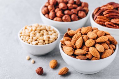 Badem, pecans, çam fıstığı ve gri arka plan üzerinde beyaz kase fındık. Fındık karışımı. Sağlıklı gıda ve snack.