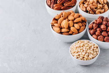 Çam fıstığı, badem, pecans, ceviz ve fındık gri arka plan üzerinde beyaz kase. Karışık kuruyemiş. Sağlıklı gıda ve snack. Kopya alanı