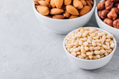 Çam fıstığı, badem ve fındık gri arka plan üzerinde beyaz kase. Fındık karışımı. Sağlıklı gıda ve snack. Kopya alanı