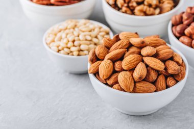 Badem, pecans, ceviz, çam fıstığı ve gri arka plan üzerinde beyaz kase fındık. Fındık ürün yelpazesine. Sağlıklı gıda ve snack. Kopya alanı