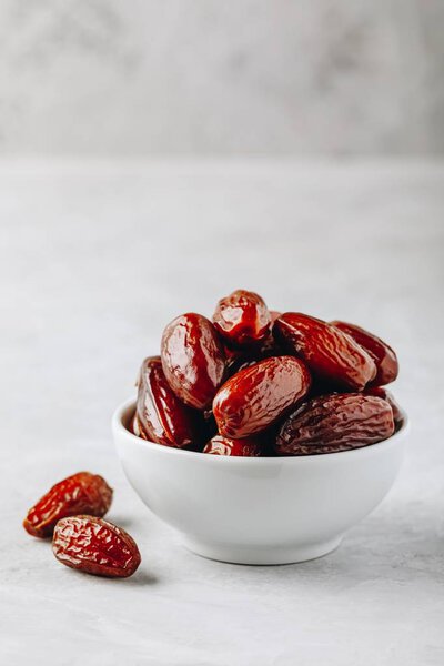 Dried dates in white bowl on grey stone background