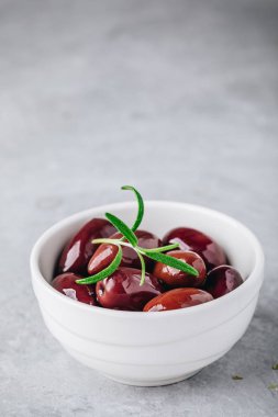 Taze organik siyah zeytin zeytinyağı biberiye gri taş zemin üzerine beyaz kase. 