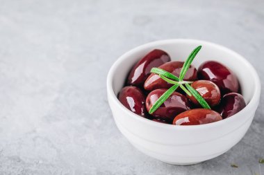 Taze organik siyah zeytin zeytinyağı biberiye gri taş zemin üzerine beyaz kase. 