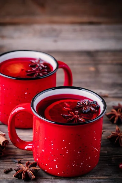 Spiced Pomegranate Apple Cider Mulled Wine Sangria in red mugs on wooden background. Hot drinks for Christmas.