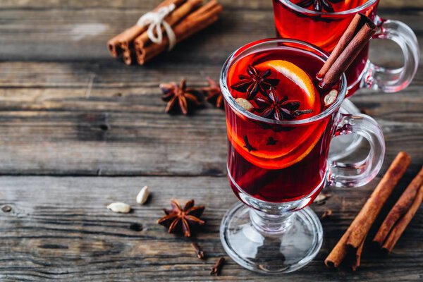 Mulled red wine with spices and orange in glass on a wooden rustic background. Homemade Christmas drink.