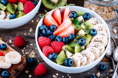 Sağlıklı kahvaltı kase granola ahududu, çilek, yaban mersini, muz, kivi ve chia tohum ahşap arka plan üzerinde