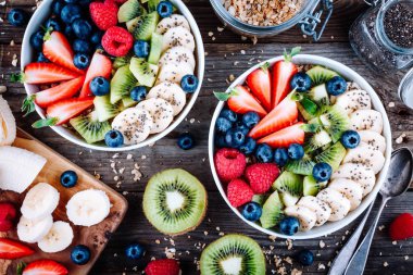 Sağlıklı kahvaltı kase granola ahududu, çilek, yaban mersini, muz, kivi ve chia tohum ahşap arka plan üzerinde