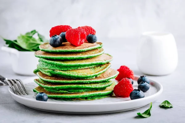 Healthy green spinach pancakes with raspberries, blueberries and honey for breakfast.