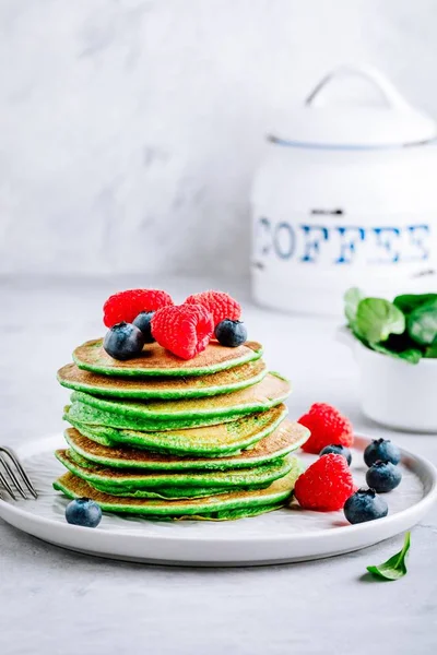 Healthy green spinach pancakes with raspberries, blueberries and honey for breakfast.