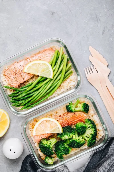 Meal prep lunch box containers with grilled salmon fish, rice, green broccoli and asparagus
