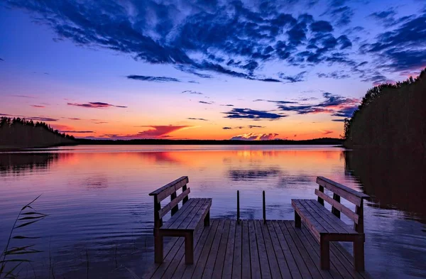 Dois bancos de madeira ou cadeiras em uma doca de madeira de frente para um lago ao pôr do sol na Finlândia — Fotografia de Stock
