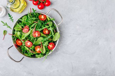 Gri taş arka planda Arugula, marul, ıspanak, pancar ve domates yeşil yaprakları ile taze salata. 