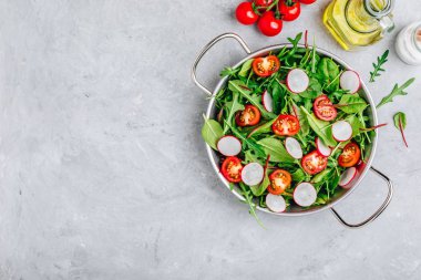 Gri taş arka planda Arugula, ıspanak, pancar, turp ve domates yeşil yaprakları ile taze salata. 