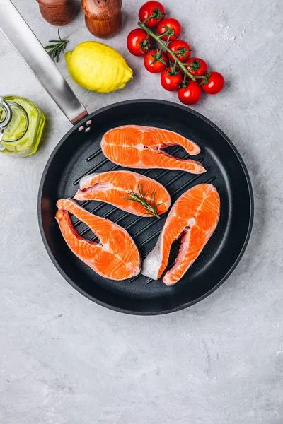 Frische rohe Lachssteaks mit Zitrone und Rosmarin und Tomaten in der Grillpfanne auf grauem Hintergrund. — Stockfoto
