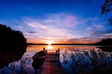 Wooden pier with fishing boat at sunset on a lake in Finland clipart