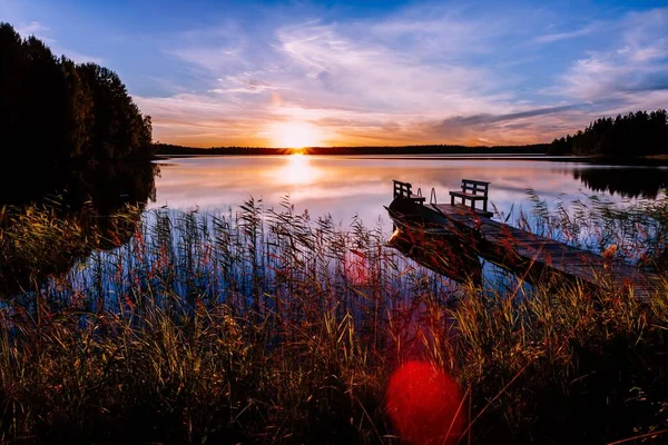 Holzsteg mit Fischerboot bei Sonnenuntergang auf einem See in Finnland — Stockfoto