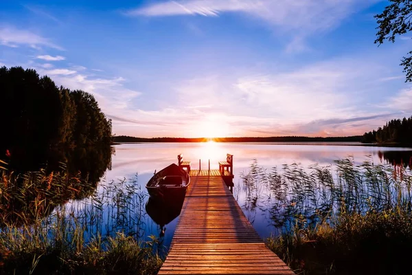 Houten pier met vissersboot bij zonsondergang op een meer in Finland — Stockfoto