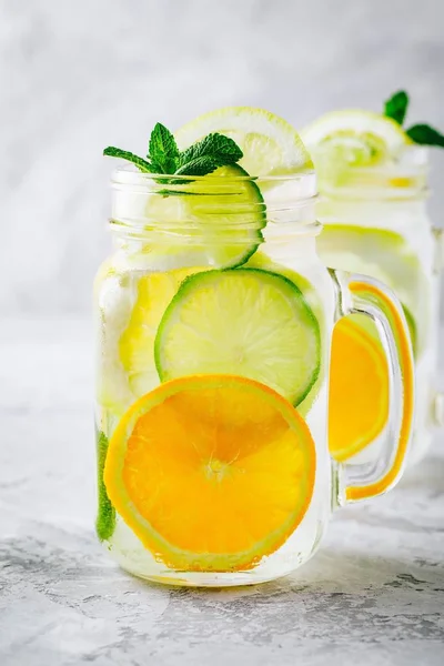 Água de desintoxicação infundida com limão, limão e laranjas fatias com hortelã. Cocktail de verão gelado em frasco de pedreiro de vidro — Fotografia de Stock