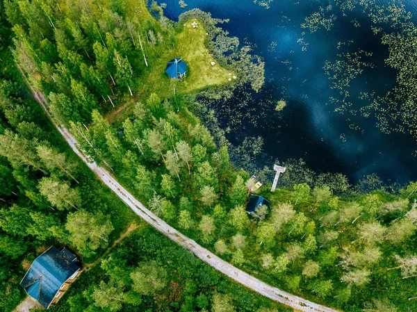 Vue aérienne d'un lac bleu avec des forêts vertes en Finlande. Maison en bois, sauna, bateaux et jetée de pêche au bord du lac . — Photo