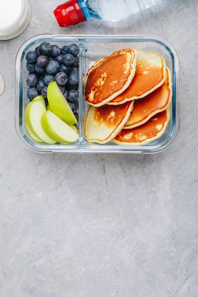 Meal prep containers with pancakes, blueberry and apple. Breakfast in lunch box. Top view.