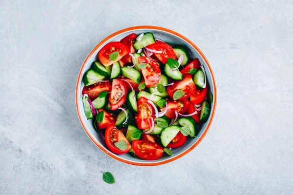Świeża sałatka letnia miska z pomidorami, ogórkami, czerwoną cebulą, bazylią i opatrunkiem oliwy. — Zdjęcie stockowe