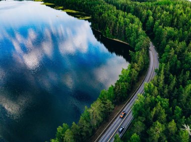 Finlandiya'da yeşil orman ve mavi göl arasındaki yolun havadan görünümü