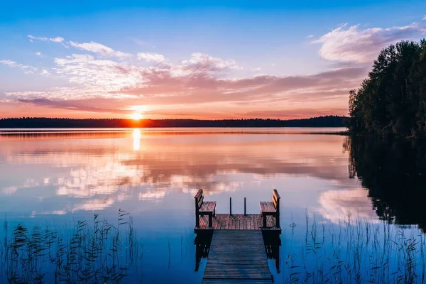 Idyllic view of the long pier with wooden bench on the lake. Sunset or sunrise over the water. — Stock Photo, Image