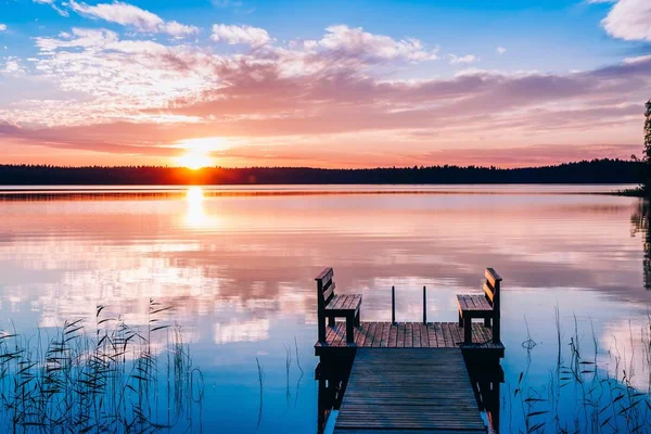 Idyllic view of the long pier with wooden bench on the lake. Sunset or sunrise over the water. — Stock Photo, Image