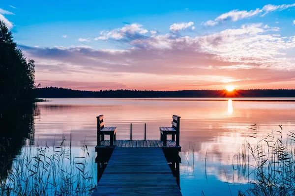 湖の上に木製のベンチと長い桟橋の牧歌的な景色。水の上の日没または日の出. — ストック写真