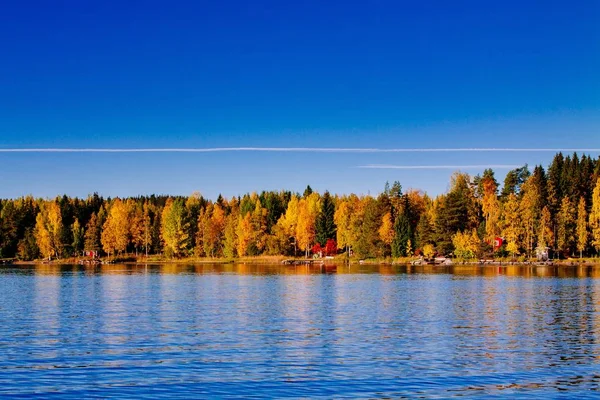Folhagem de outono, queda floresta colorida sobre lago azul com cabines vermelhas na Finlândia . — Fotografia de Stock