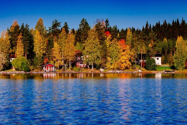 Ősz lombja, ősz színes erdei kék tóval, piros kabinnal Finnországban. — Stock Fotó
