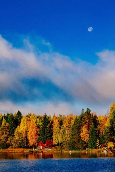 Φθινοπωρινό φύλλωμα, φθινόπωρο πολύχρωμο δάσος πάνω από τη γαλάζια λίμνη με κόκκινες καμπίνες στη Φινλανδία. — Φωτογραφία Αρχείου