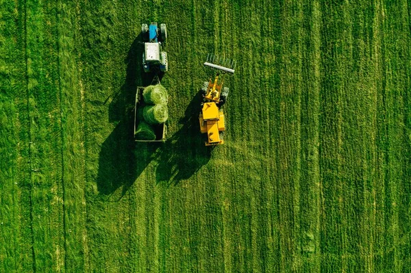 Вид с воздуха на поле для сбора урожая с трактором, движущимся из сена — стоковое фото