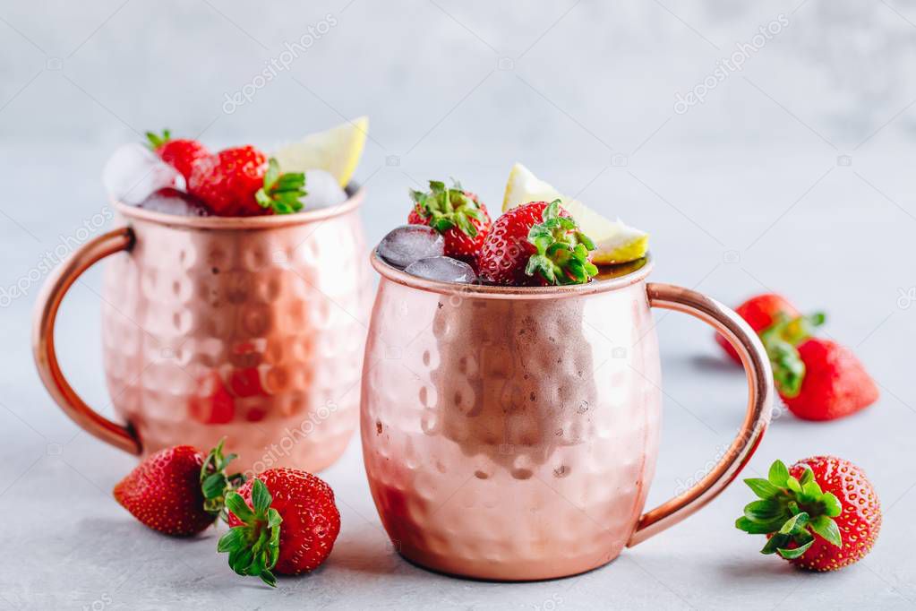 Refreshing iced Moscow mule alcoholic cocktail in copper mugs with strawberry and lemon 