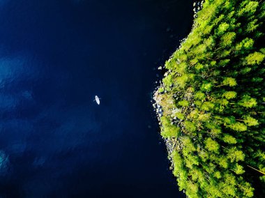 Finlandiya'da bir balıkçı teknesi ve kayalar ile yeşil ormanlar ile mavi göl havadan görünümü. 
