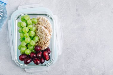 Üzüm ve gevrek ekmek ile yemek hazırlık kapları. Öğle yemeği kutusunda kahvaltı meyveleri. Üst görünüm, kopyalama alanı.