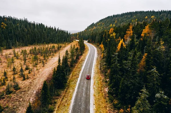 Vista aérea del primer bosque nevado de color otoñal en las montañas y una carretera con coche en Finlandia Laponia . —  Fotos de Stock