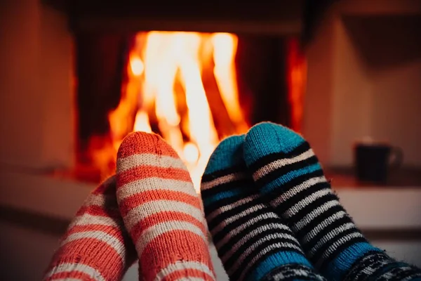 Feet in wool striped socks by the fireplace. Relaxing at Christmas fireplace on holiday evening. — Stock Photo, Image