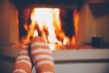 Şöminenin yanında yün çizgili çoraplı ayaklar. Tatil akşamında Noel şöminesinde dinleniyor..